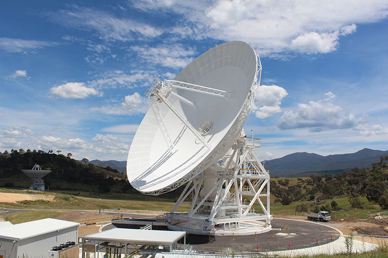 Wider shot showing DSS36 in the centre, on an angle facing to the left. DSS45 in the background to the left. Blue sky with clouds and hills in the background