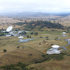 Side on aerial view of the canberra Deep Space Communication Complex, with hills and misty cloud in the background.