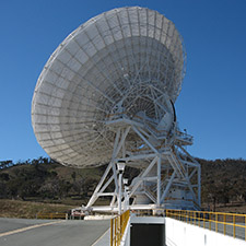 The antenna Deep Space Station 34 facing away from the camera, showing the driveway that leads under the antenna, hills and blue sky in the background.