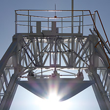 The subreflector of Deep Space Station 34 with part of the quad leg structure leading to it, the Sun shining out from behind the bottom of the subreflector dish.