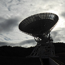 Deep Space Station 35 in shadow with a bright cloudy sky behind.