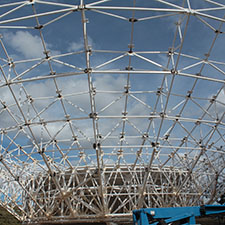 The ribs of the dish structure with no panels covering them, blue sky with clouds behind.