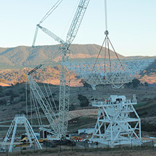 A crane lifting the dish for Deep Space Station 35 on to its pedestal structure. Quad legs sitting on the left, hills behind being lit up by sunrise.
