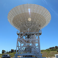 Deep Space Station 36 facing straight up showing hills and blue sky with sun rays.