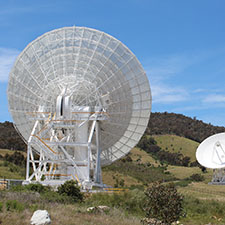 Deep Space Station 36 from the back showing the pedestal and back of the dish, hills and Deep Space Station 35 in the background with blue sky.