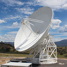 Deep Space Station 36 on an angle showing the surface of the dish, blue sky with clouds and hills in the background.