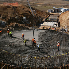 Concrete being poured onto the metal structured circular base of the pedestal. People standing on the structure.