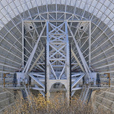 Back of the dish structure of Deep Space Station 43 with the top of a tree at the bottom of the image.