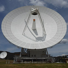 Deep Space Station 45 on an angle, showing the dish surface and receiver structure, DSS-34 in the far background.