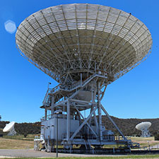 Antenna Deep Space Station 45 facing up with a very blue sky and two other antennas in the background.
