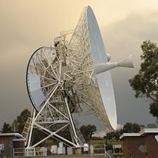 Deep Space Station 46 on an angle facing right, showing part of its receiver cone, with stormy clouds behind.