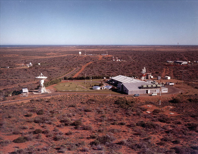 Aerial view of Carnarvon showing red dirt with plants, several buildings, roads and an antenna.