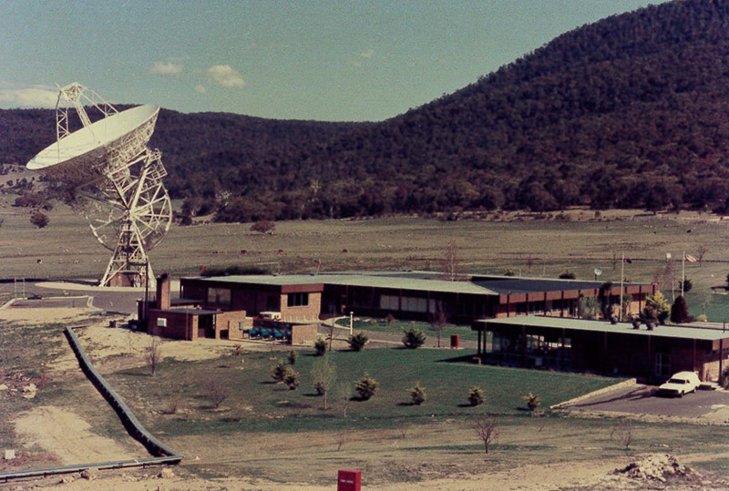 Building with an antenna to the left of it on an angle and hills behind