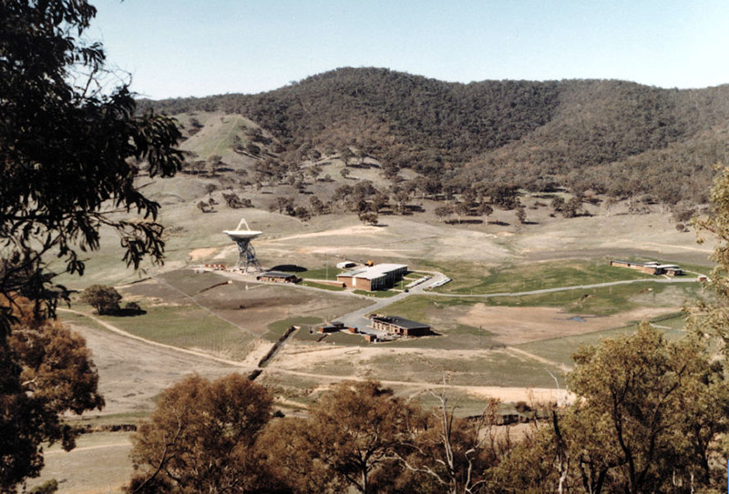 A valley surrounded by hills with an antenna and some buildings in it.