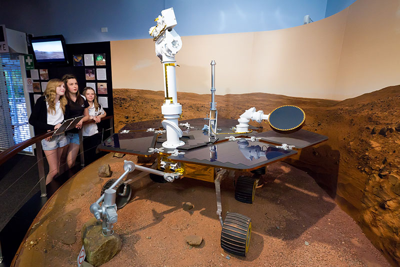 Three teenage girls looking at a model of the Mars Exploration Rovers